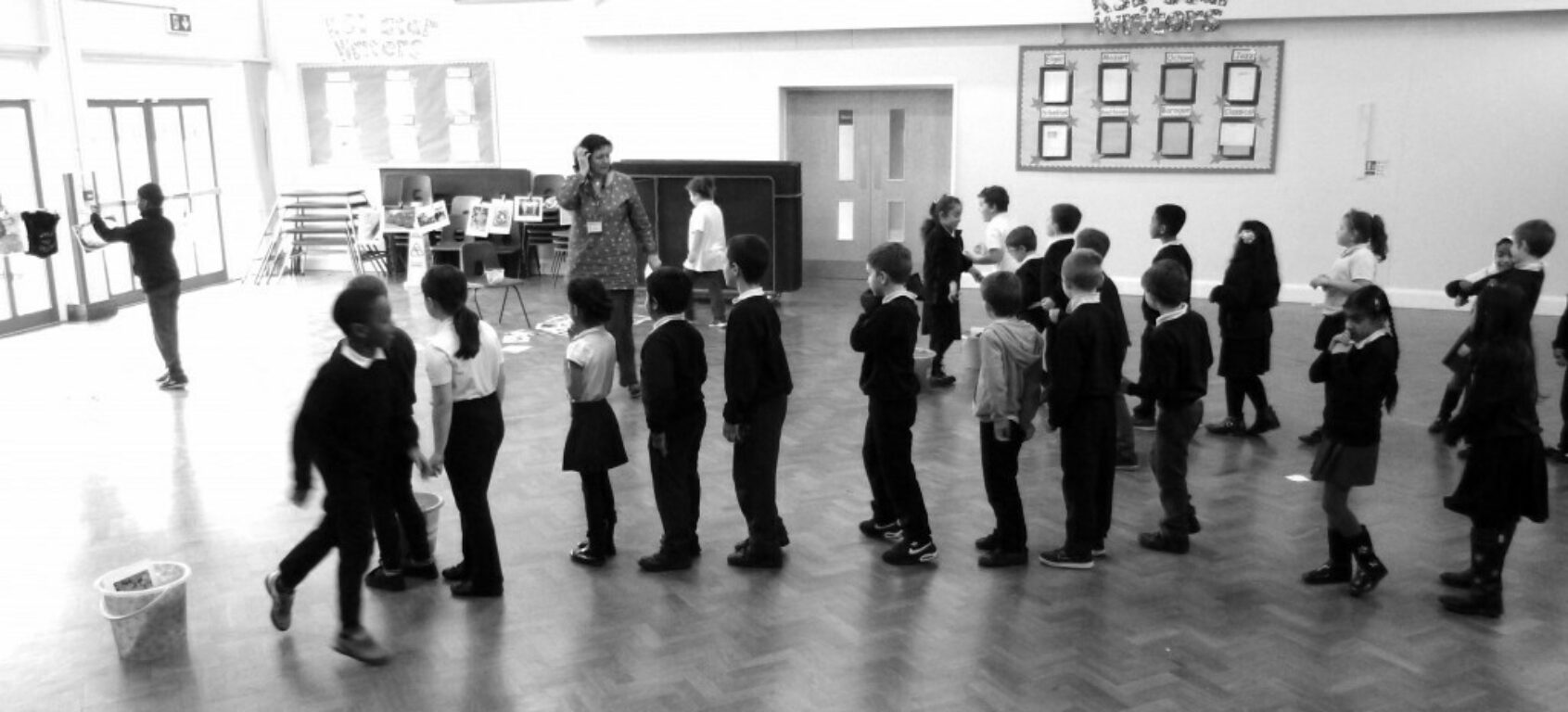Black and white photograph of children in a school hall lining up to participate in an activity.