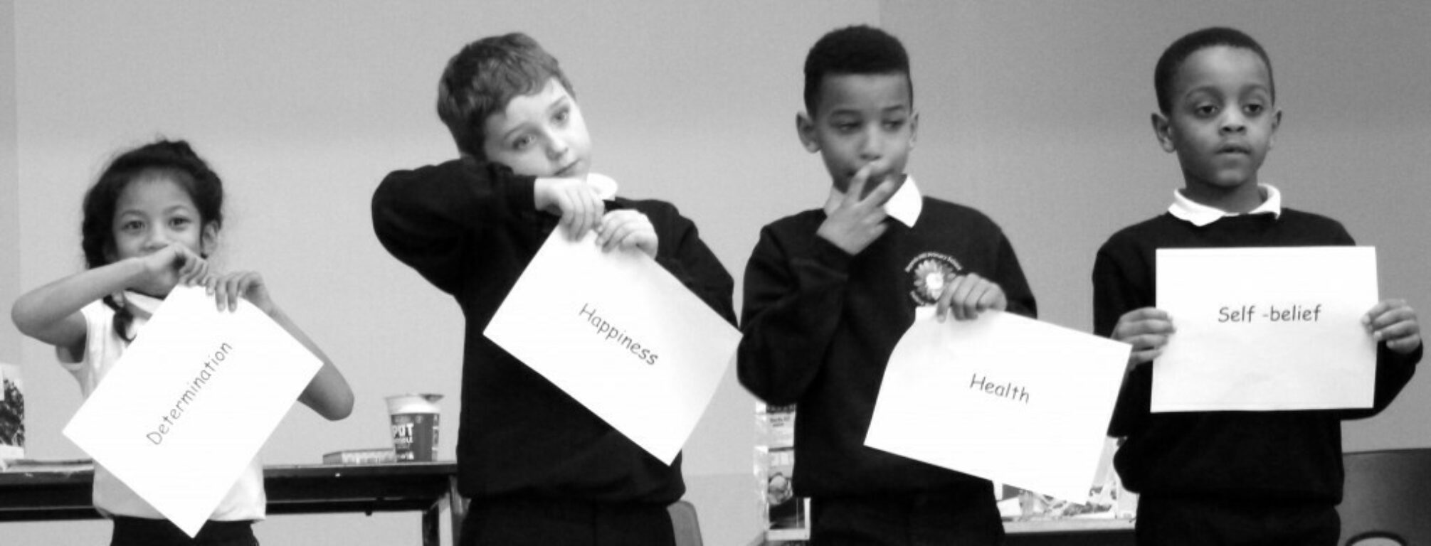 Black and white photo of four children holding cards reading different relevant words to the project.